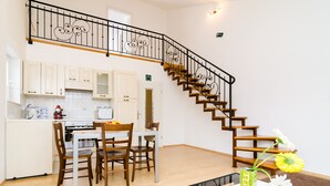 Una cocina moderna con armarios blancos, una mesa de comedor con sillas y una escalera de madera con barandilla decorativa.