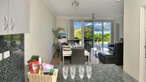 A modern kitchen with granite countertops, a dining area with a view, and a living space with a sofa and a TV.