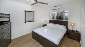 A bedroom with a bed, a dresser, a TV, a ceiling fan, a mirror, and a nightstand with a lamp.