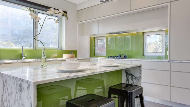 Een moderne keuken met een marmeren eiland, groene accenten en een raam met natuurlijk licht.