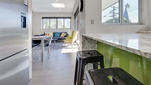 Een moderne keuken met een marmeren aanrecht, een eethoek met een bank en stoelen, en grote ramen die zorgen voor natuurlijk licht.