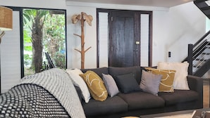 A modern living room with a dark sofa, multiple cushions, a coffee table, and a staircase. - The Edge 13 Marine Parade, Newell Beach QLD 4873 (Newell)