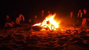 Un gruppo di persone sedute attorno a un fuoco da campo su una spiaggia sabbiosa di notte.