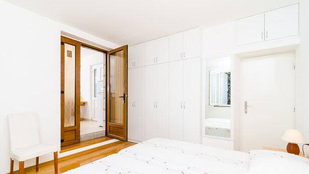 Ein Schlafzimmer mit einem Bett, einem Sessel, einem Kleiderschrank und einer Tür zu einem weiteren Raum.