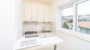 Eine kleine Küche mit weißen Schränken, einem Spülbecken und einem Fenster mit Blick auf eine Wohngegend.