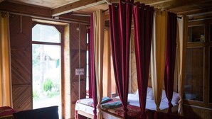 A wooden room with a bed, a table, and curtains. - Lato The Huts River Touch Guesthouse  (Kullu)