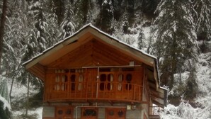 A wooden chalet with multiple windows and a balcony, surrounded by snow-covered trees. - Lato The Huts River Touch Guesthouse  (Kullu)