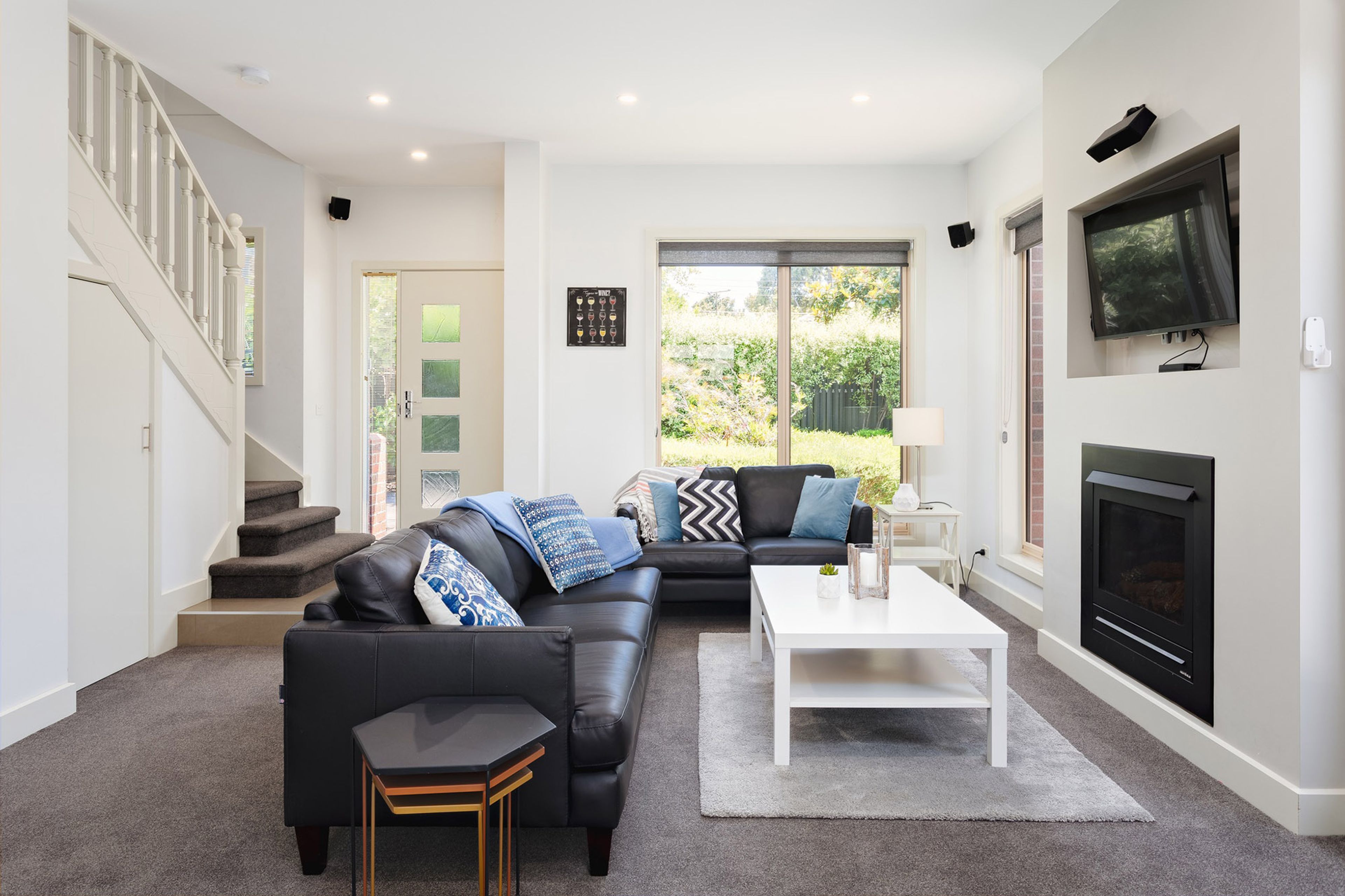 A modern living room with a black leather sofa, a white coffee table, and a fireplace.