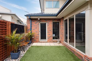 A residential property with a brick exterior, a small front yard with artificial grass, a wooden fence, and potted plants.