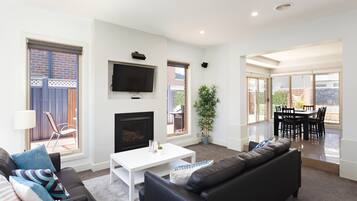 A modern living room with a fireplace, a flat-screen TV, and a dining area with a table and chairs.