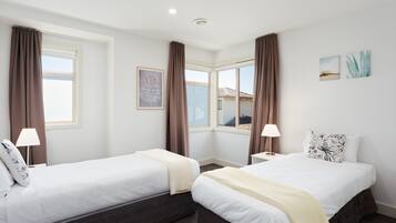 A hotel room with two beds, a window, a painting, and a lamp.