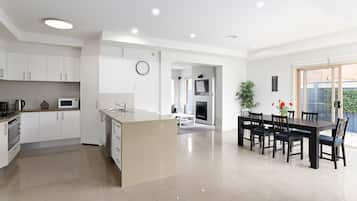 A modern kitchen with white cabinets, a central island, and a dining area with a black table and chairs.