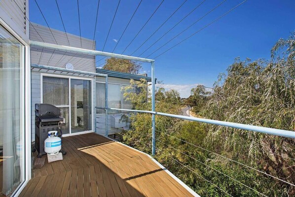 A balcony with a grill and propane tank, overlooking a garden with dense foliage.
