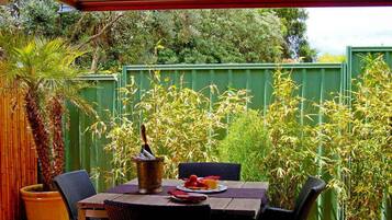 Une terrasse avec une table dressée pour deux personnes, entourée d’une végétation luxuriante et d’une clôture en bambou.