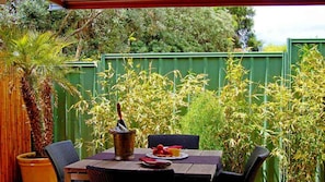 Une terrasse avec une table dressée pour deux personnes, entourée d’une végétation luxuriante et d’une clôture en bambou.