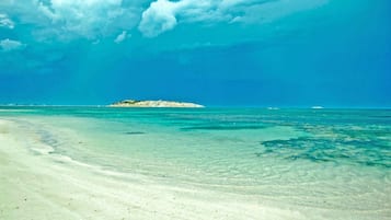 Une plage à l’eau turquoise et limpide, un rivage sablonneux et une petite île qui se profile à l’horizon.