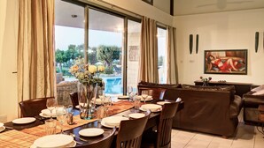 A dining area with a table set for six, large windows, and a painting on the wall. - Villa Nasia (Neo Chorio)