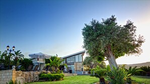 A modern two-story house with a stone wall, a large tree, and a well-maintained lawn. - Villa Nasia (Neo Chorio)