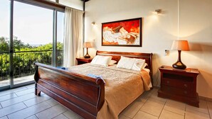 A bedroom with a large bed, two bedside tables, a painting on the wall, and a balcony with a view. - Villa Nasia (Neo Chorio)