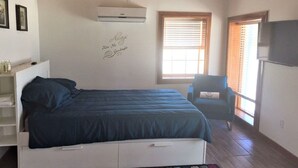 Un dormitorio con una cama, una silla, un televisor y una ventana.