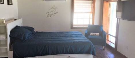 A bedroom with a bed, a chair, a TV, and a window.
