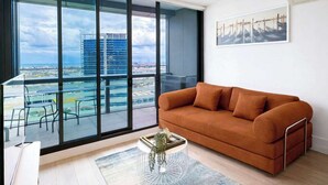 A modern living room with a large window, a brown sofa, and a view of a cityscape.