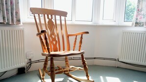 Ein Schaukelstuhl in einem Zimmer mit Heizkörper, Fenster und Steckdose.