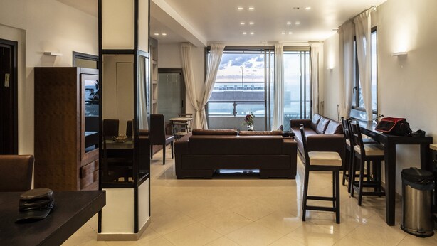 A modern living room with a sofa, dining table, and chairs. There is a view of a cityscape through large windows. - Perfect location  with panoramic sea view facing Gordon Beach (Tel Aviv-Yafo)