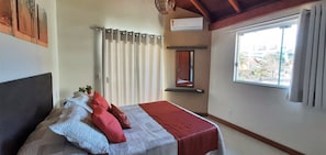 A bedroom with a bed, a window, a wall-mounted air conditioner, and a door.