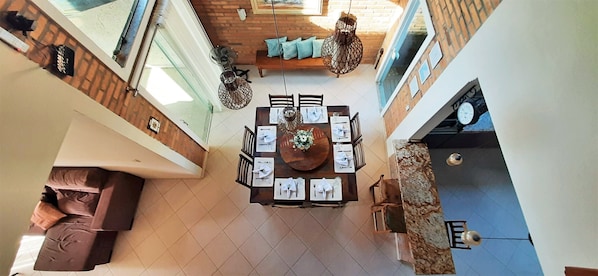 A dining area with a round table set for four, surrounded by chairs. There is a sofa and a hanging light fixture above the table. - House with 4 bedrooms and a heated pool in Bombinhas. (Bombas)