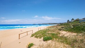 A sandy beach with a wooden fence, ocean waves, and coastal vegetation. - The Pavillion 1 - Beachfront (Wamberal)