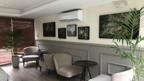 Uma sala de estar moderna com um sofá, duas poltronas, uma mesa de centro e um vaso de planta. Há um ar-condicionado fixado na parede e quadros acima da área de estar.