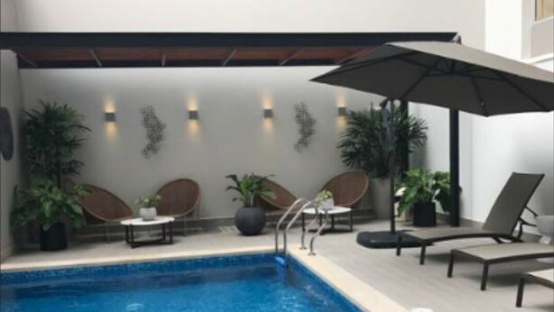 Uma área interna de piscina moderna com água azul cristalina, cadeiras de descanso e plantas em vasos.