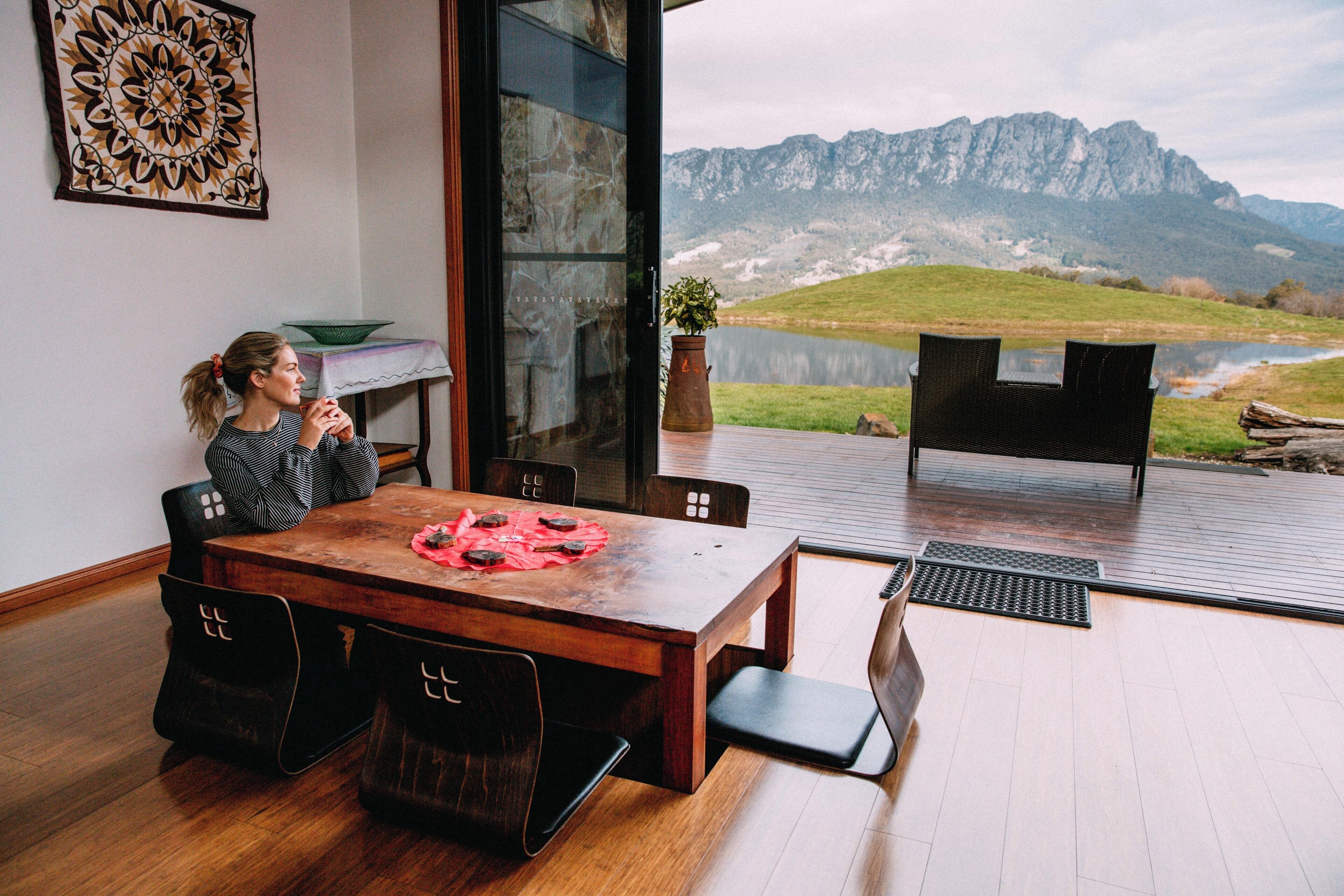 A dining area with a wooden table and chairs, a view of mountains, and a glass door leading to an outdoor deck.