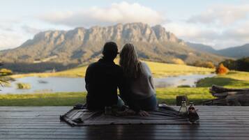 A couple sitting on a wooden deck overlooking a lake with mountains in the background.