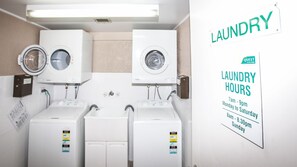 A laundry area with two washing machines and dryers, a sign indicating laundry hours, and a wall-mounted sign with the word 'LAUNDRY'.
