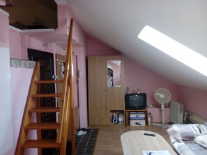Ett rum med rosa väggar, en trästege, en tv, en fläkt och en säng.