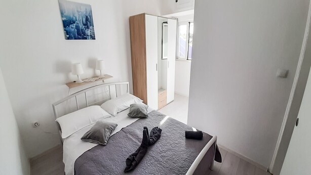 A bedroom with a bed, pillows, a bedside table with lamps, a wardrobe, and a cityscape painting on the wall. - Cozy apartment for 4 (Marina)
