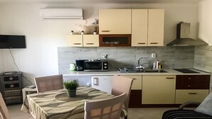 A compact kitchen with a microwave, toaster, and sink. There is a dining table with chairs and a small potted plant. - Cozy apartment for 4 (Marina)