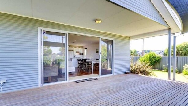 A modern house with a covered patio, sliding glass doors leading to an open kitchen, and a wooden deck.