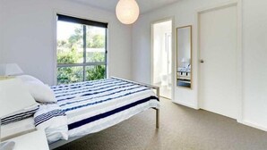 A bedroom with a bed, a window, a door, and a hanging light fixture.