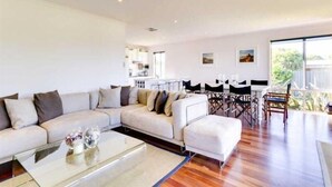 A spacious living area with a large L-shaped sofa, a glass coffee table, and a dining table with chairs.