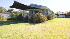 A modern house with a large shaded patio area, surrounded by a well-maintained lawn and various plants.