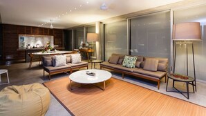 Ein modernes Wohnzimmer mit einer Couch, einem Couchtisch und einem Essbereich, wobei im Hintergrund eine Küche zu sehen ist.