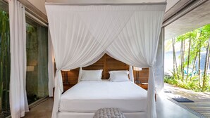 Ein großes Bett mit Baldachin, ein runder Hocker und Blick auf Palmen durch eine Glastür.