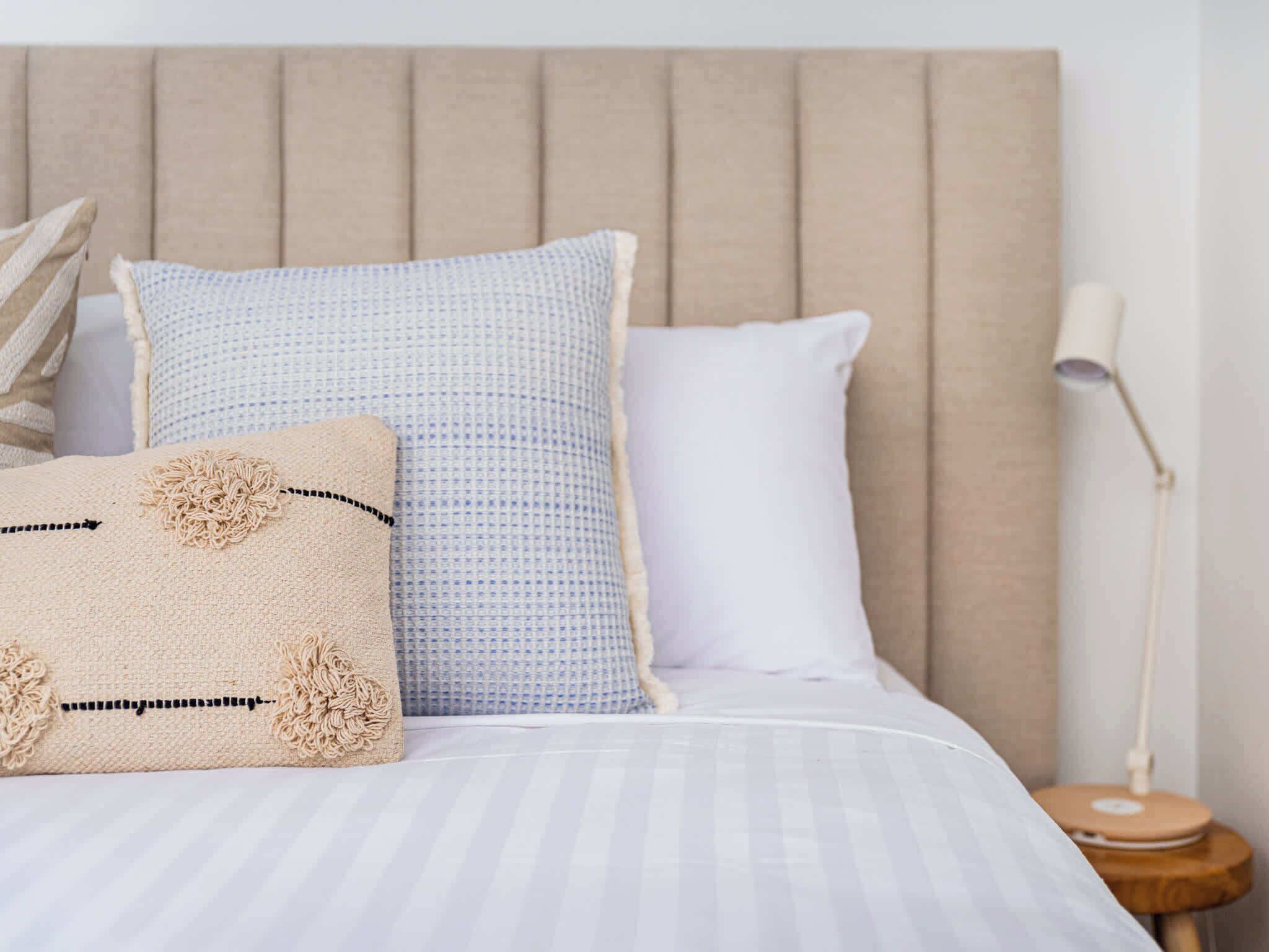 Een bed met een gestreepte spreideken, een beige hoofdbord en twee kussens met een blauw-beige patroon.