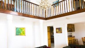 Un salon spacieux avec deux canapés verts, un escalier en bois et un lustre.