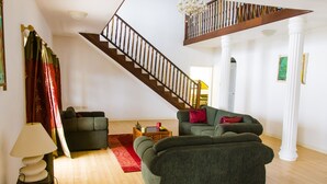 Un salon avec un escalier, des canapés verts, un plancher en bois et un lustre.