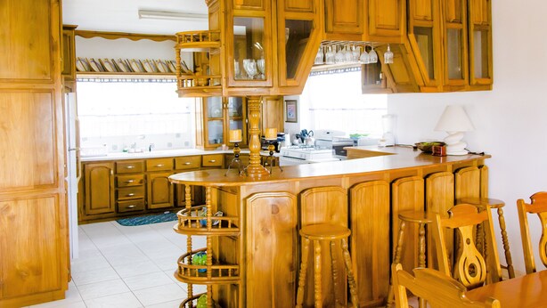 Une cuisine avec des meubles en bois, un îlot central doté de tabourets et une table à manger.