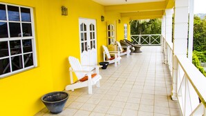 Un balcon abrité, doté de chaises blanches et d’un sol carrelé, entouré de murs jaunes et de portes blanches.